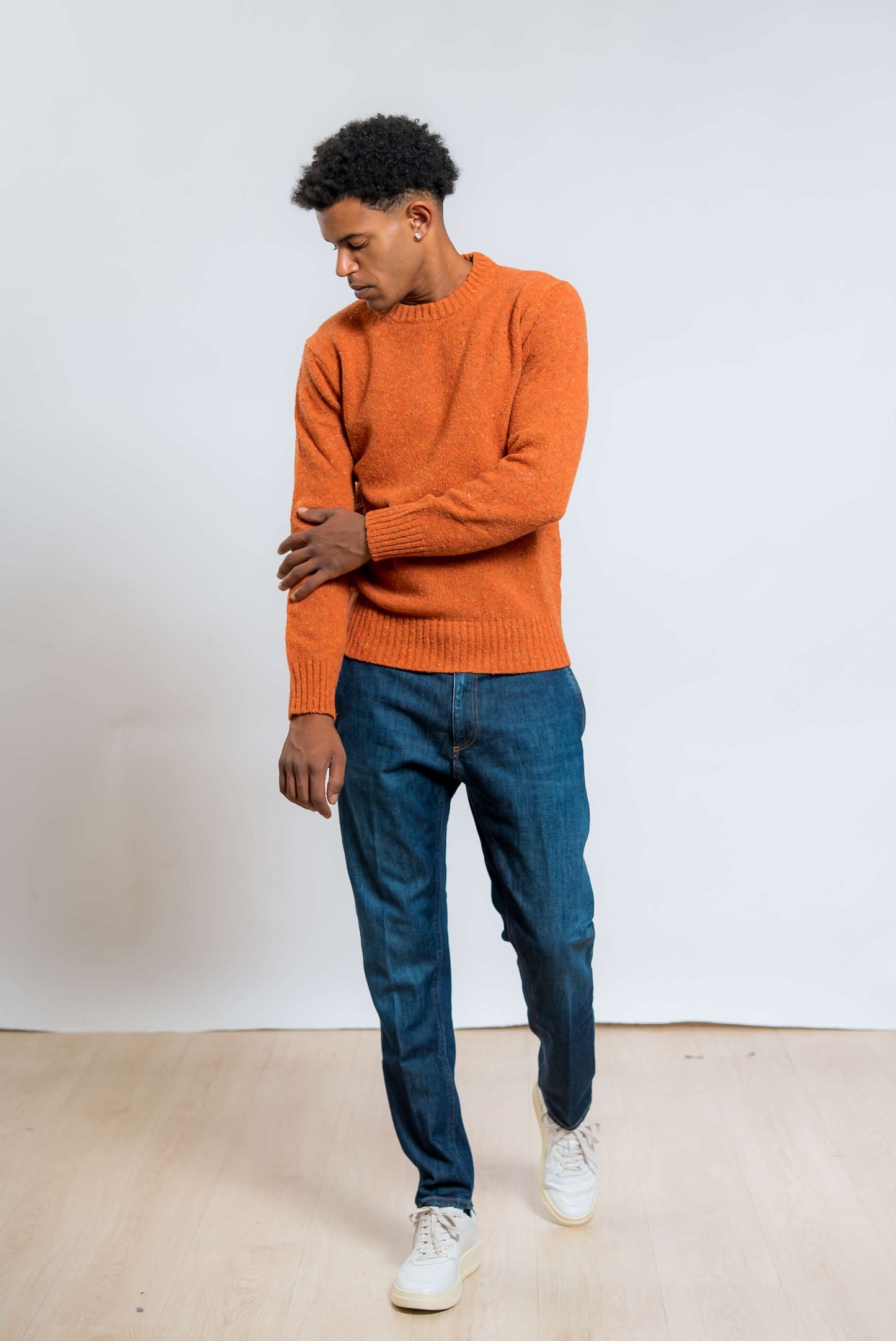 maglione a girocollo in lana boucle arancione di kangra abbinato ad un jeans blu e una sneakers bianca