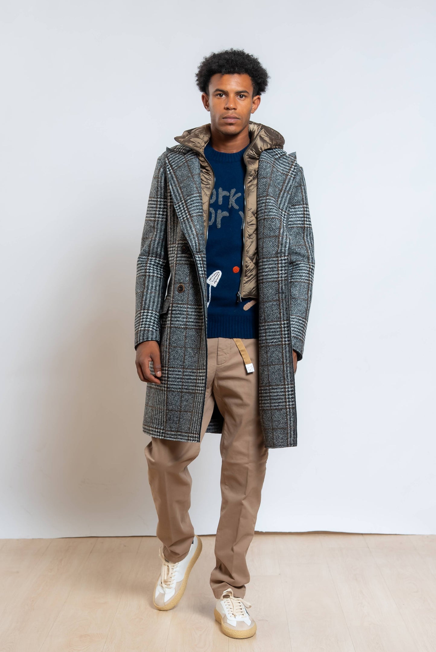 Cappotto fenit di bob in pied de poule grigio e nero abbinato a maglione blu e pantaloni beige