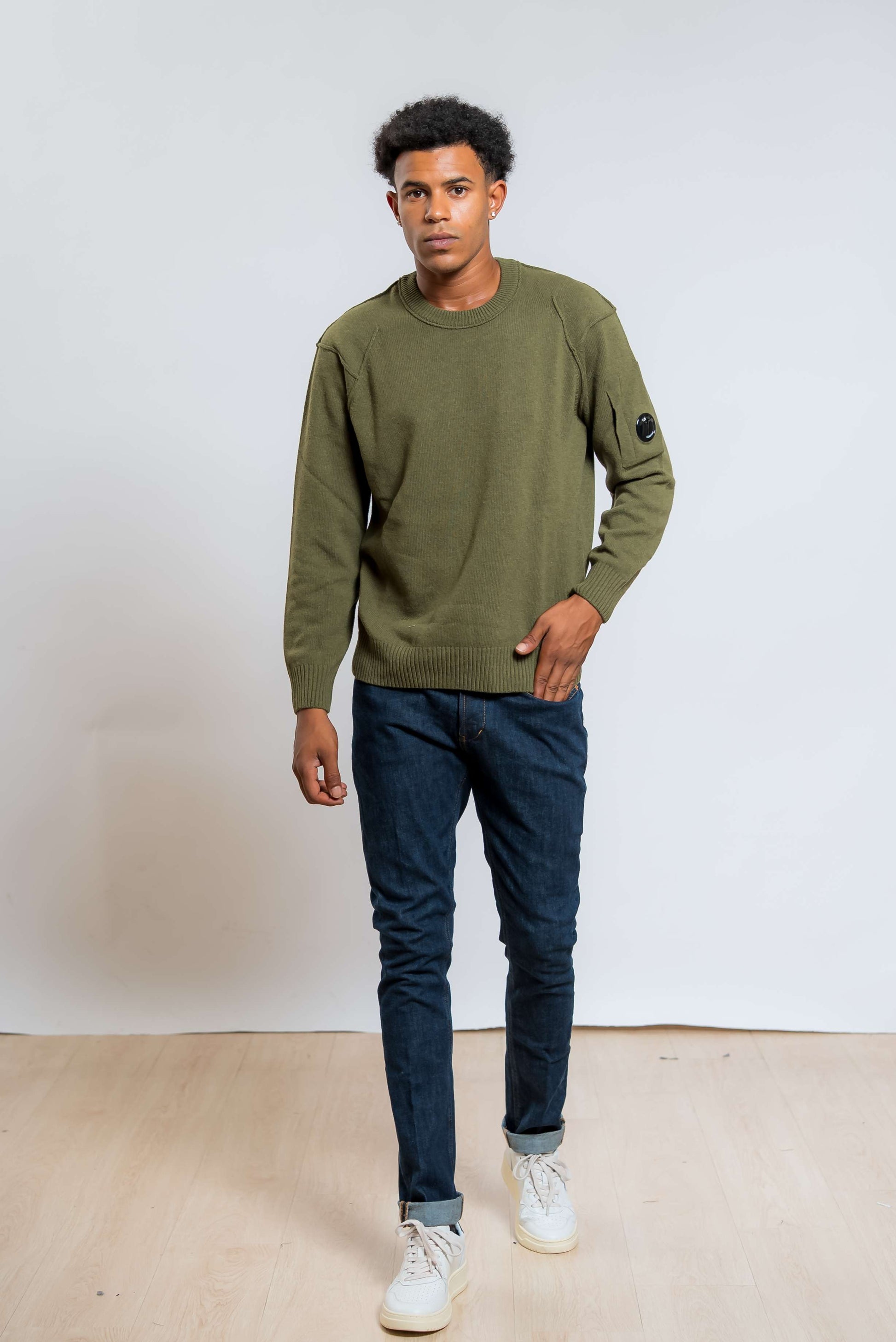 cp company maglione lambswool in lana verde abbinato ad un jeans blu e una sneakers bianca