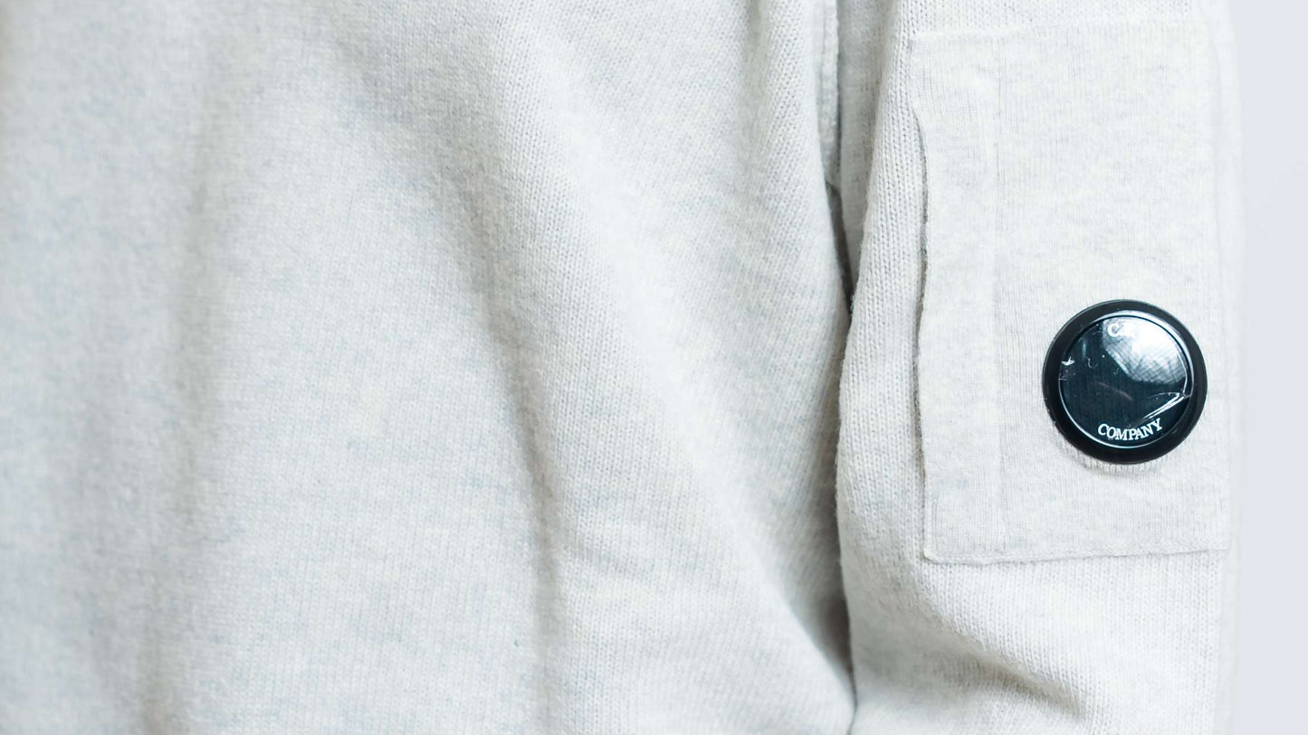 dettaglio del taschino con cp company lens e cuciture in rilievo del maglione lambswool in lana grigia