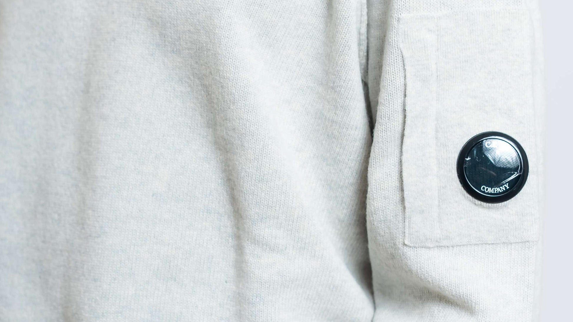 dettaglio del taschino con cp company lens e cuciture in rilievo del maglione lambswool in lana grigia